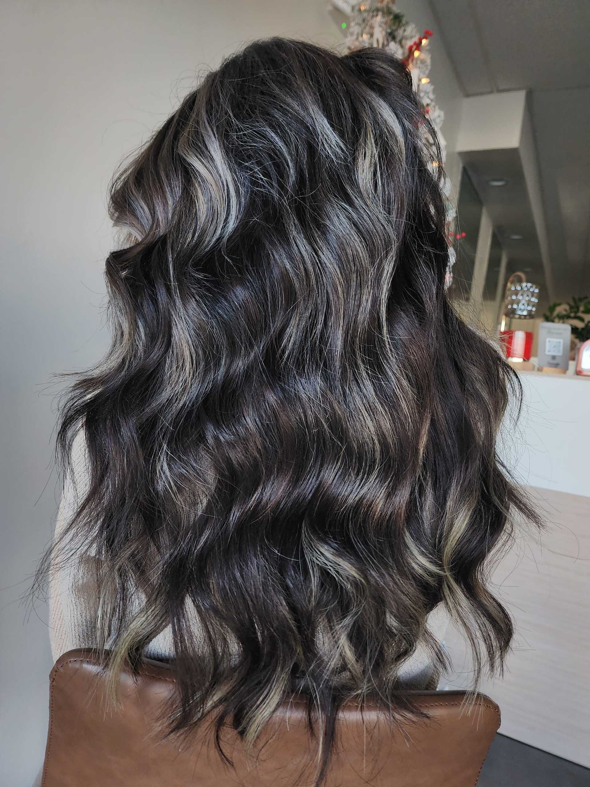 Long wavy hair with dark brown and blonde highlights, styled elegantly in a salon.