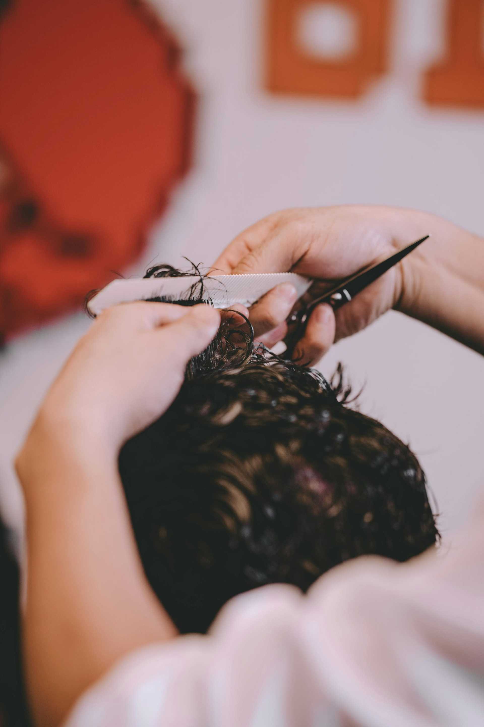 Man getting a haircut at a barber shop, close-up of hands with scissors and comb.
