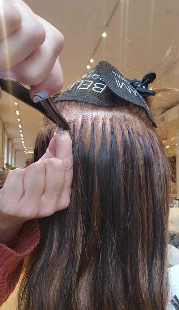 Hairdresser applying extensions to a client's hair with a weaving technique in a salon.