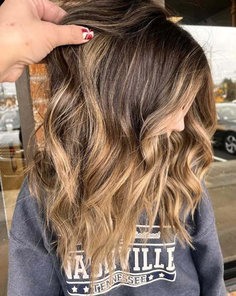 Highlighted wavy hairstyle with brown and blonde tones, person in a graphic sweatshirt.